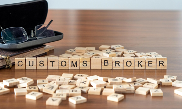 customs broker word or concept represented by wooden letter tiles on a wooden table with glasses and a book Scrabble tiles spelling "Customs Broker" on a wooden table