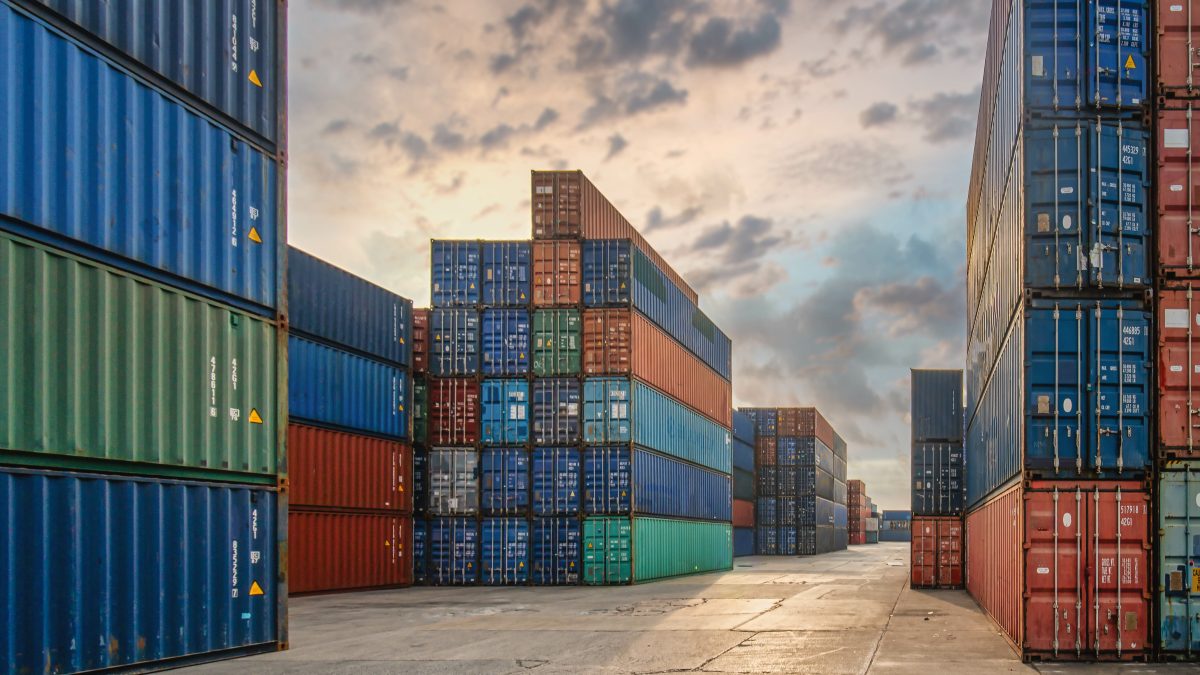 Stacks of colorful shipping containers at a port under a cloudy sky