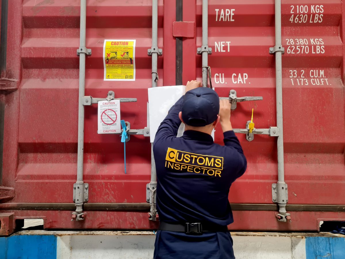 Customs inspector examining a labeled shipping container with caution signs and weight markings.